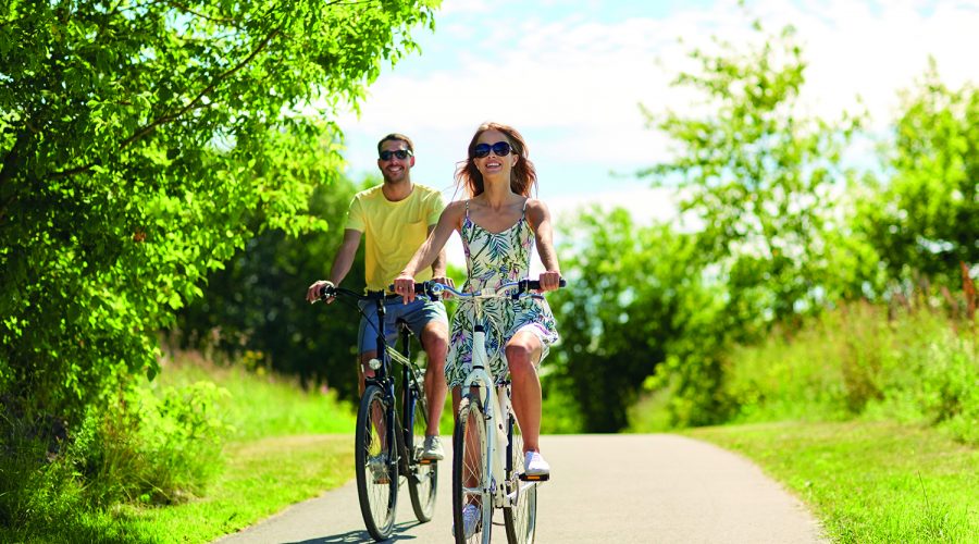 people, leisure and lifestyle concept - happy young couple riding bicycles along road in summer